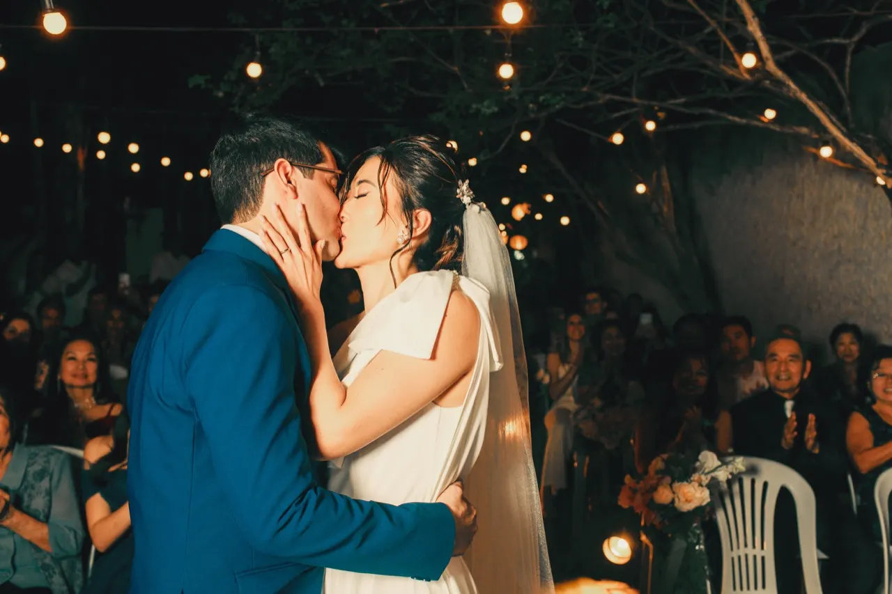 Newlyweds kissing beneath string lights